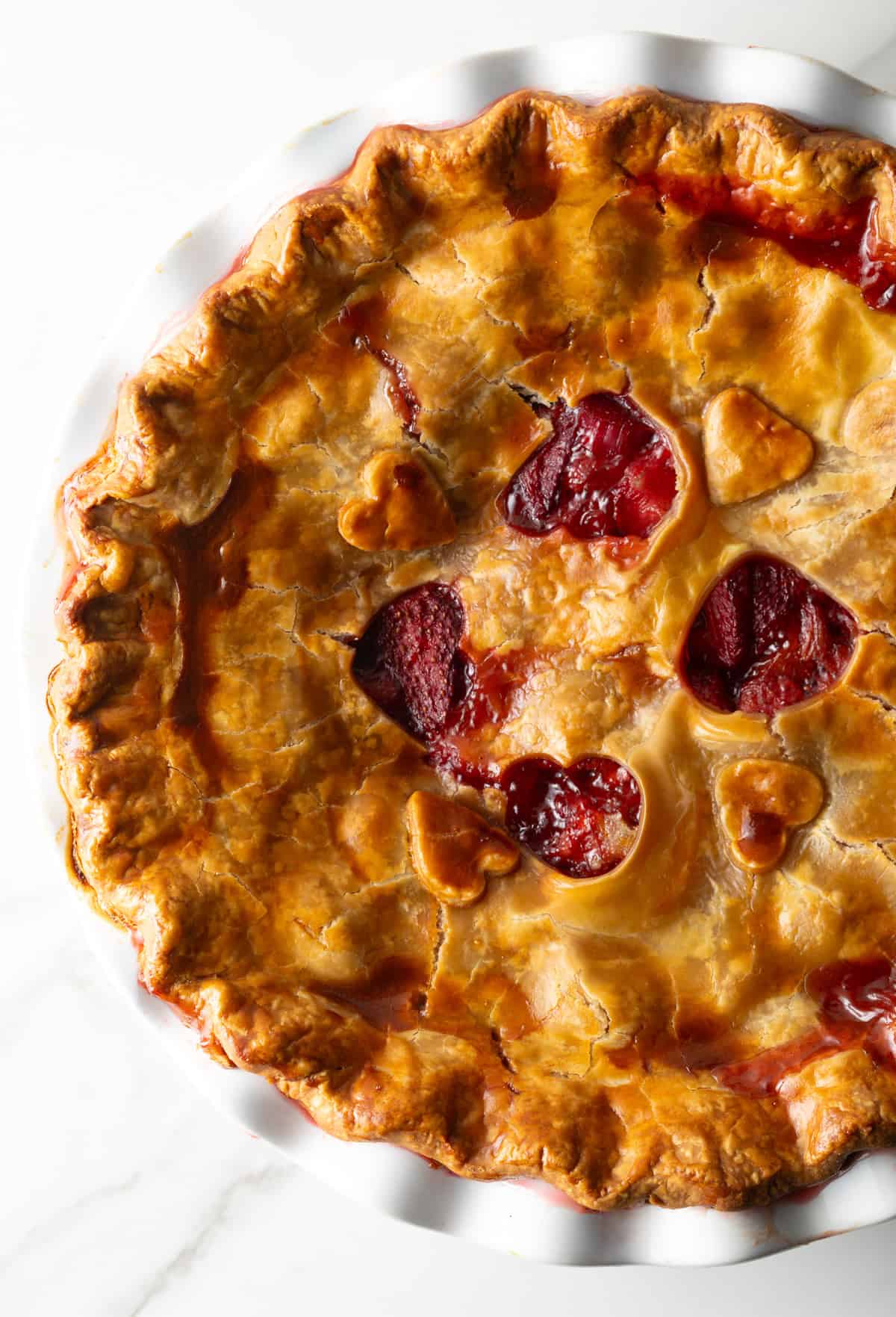A freshly baked homemade strawberry rhubarb pie with heart shapes cut in the center of the pie.