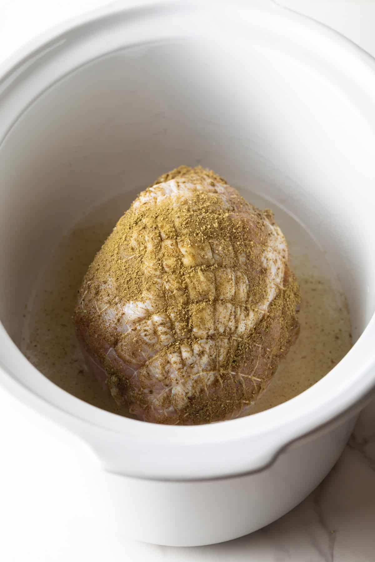 A turkey breast in the slow cooker topped with seasonings.