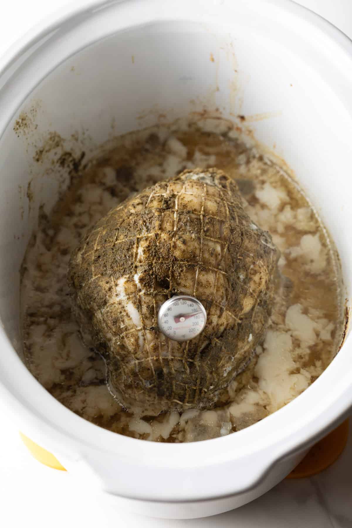 A cooked turkey breast in a crock pot with a meat thermometer sticking out of the top.