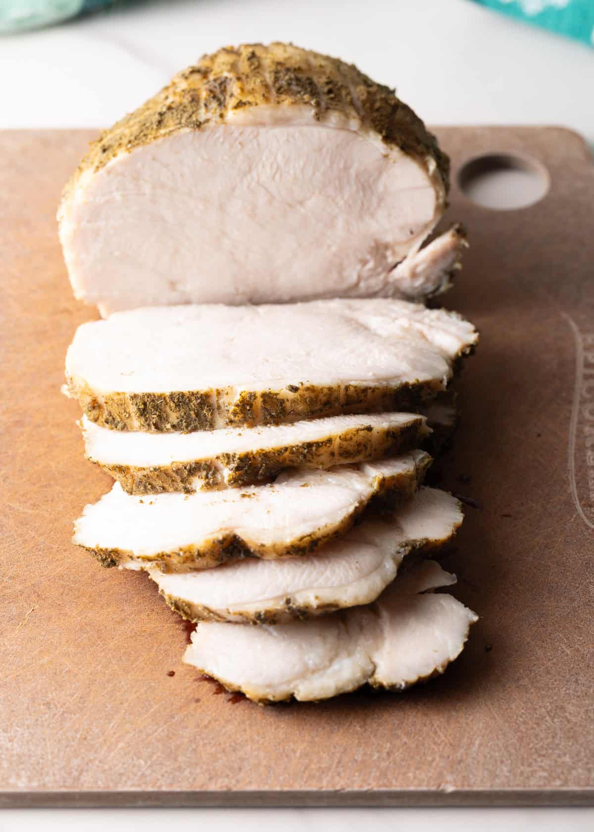 Sliced slow cooker turkey breast sitting on a cutting board.