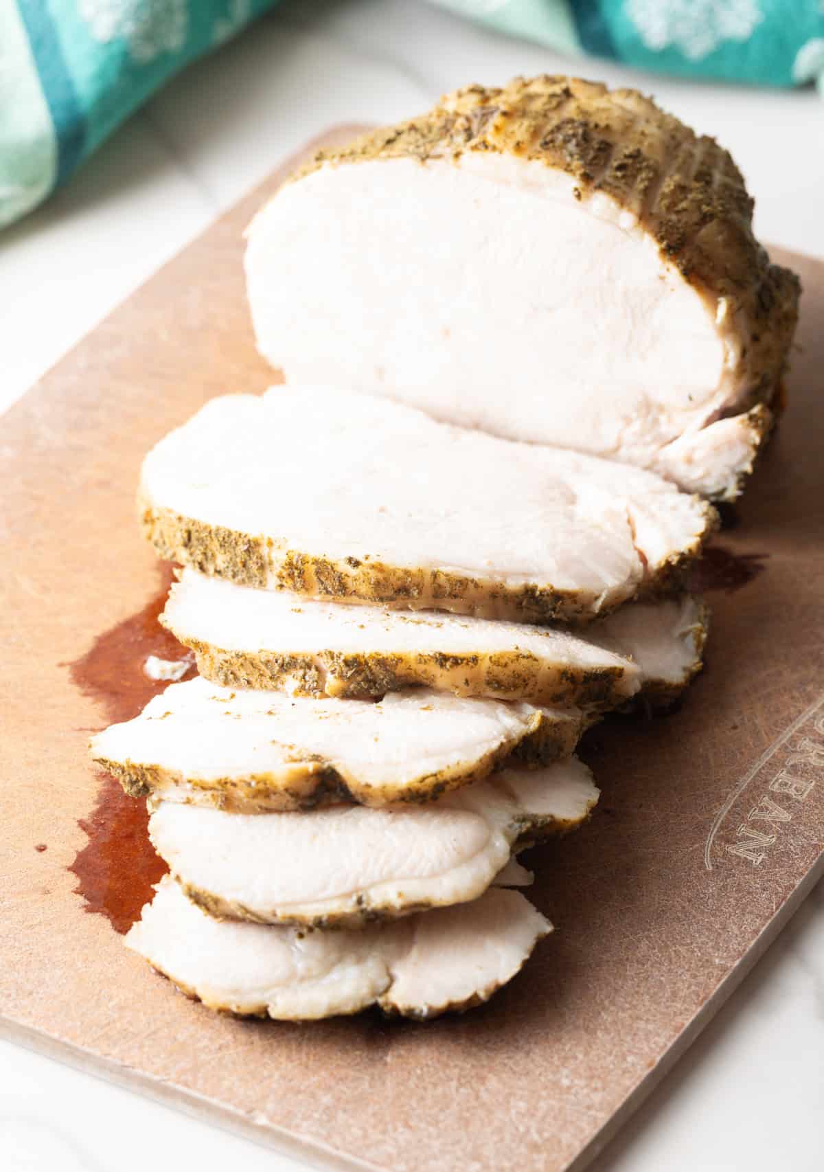 A sliced slow cooker turkey breast sitting on a wooden cutting board.