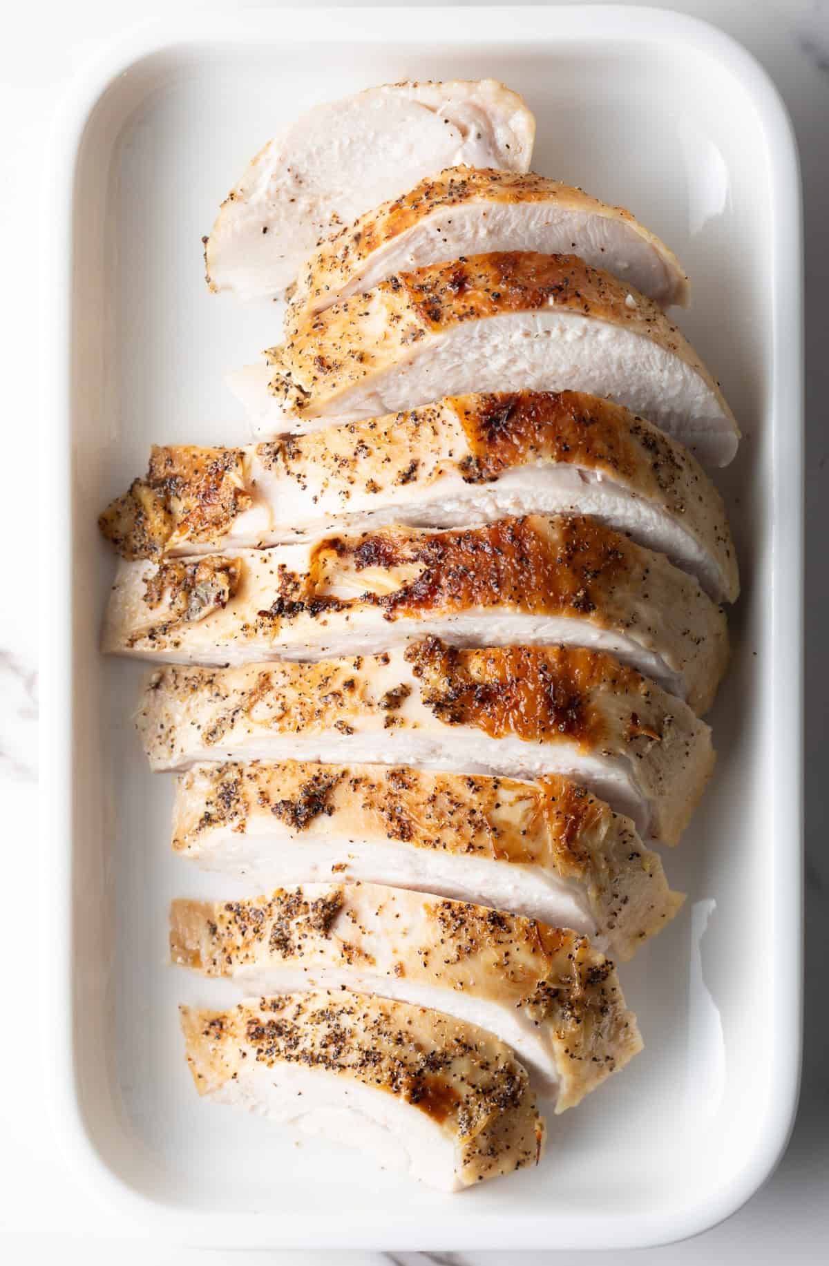 A sliced turkey breast in a white dish that has been prepared in the crock pot.