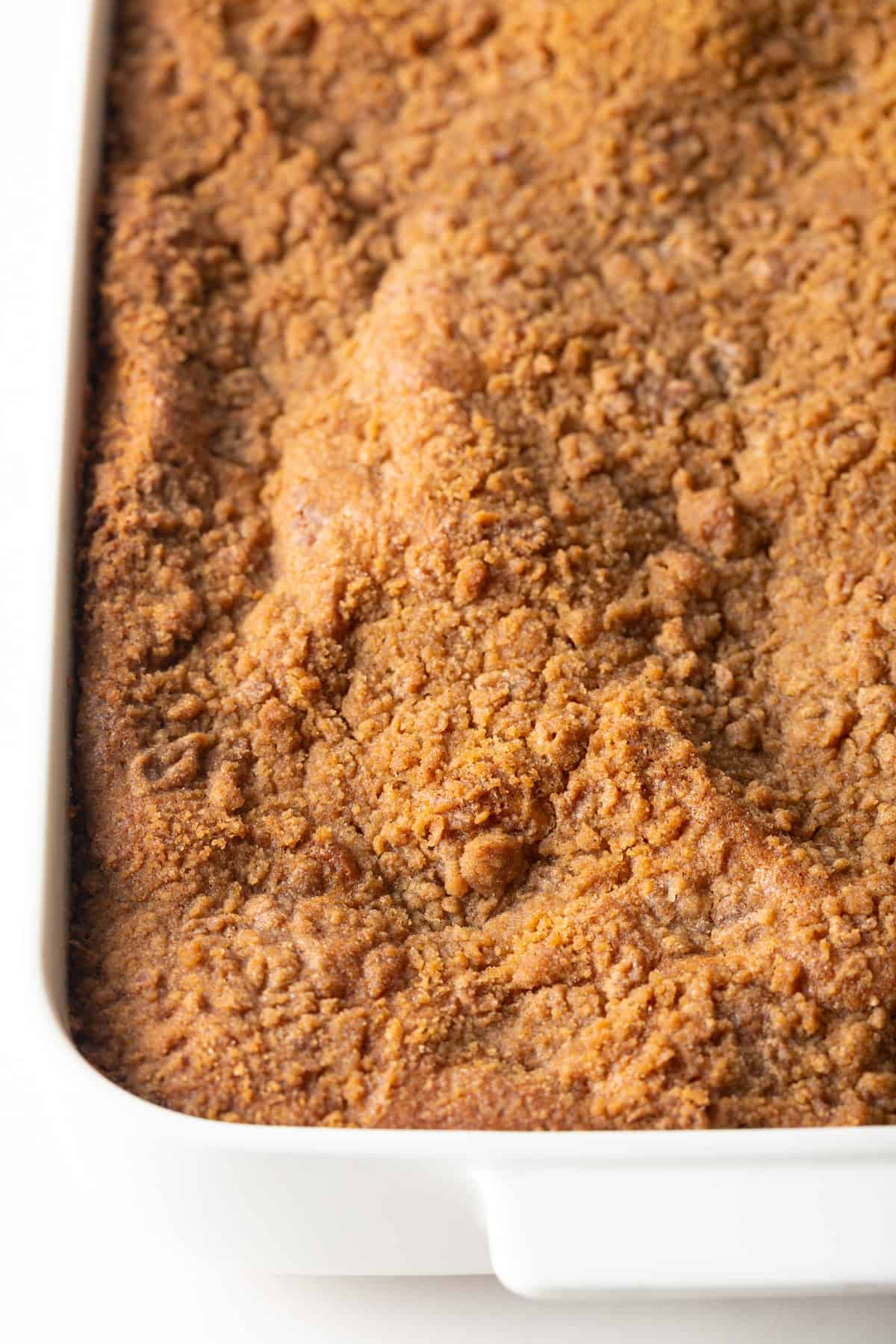 An easy coffee cake with sour cream topped with cinnamon crumble in a white baking pan.