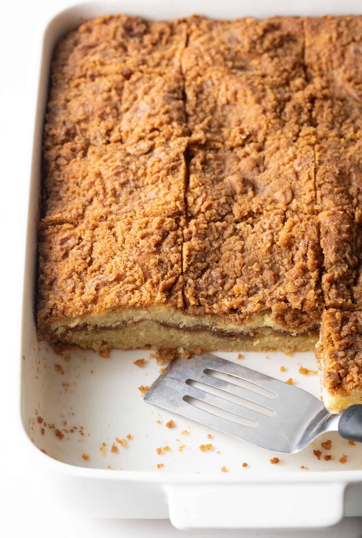 An easy cinnamon coffee cake recipe in a white baking pan, with slices taken out at the end.