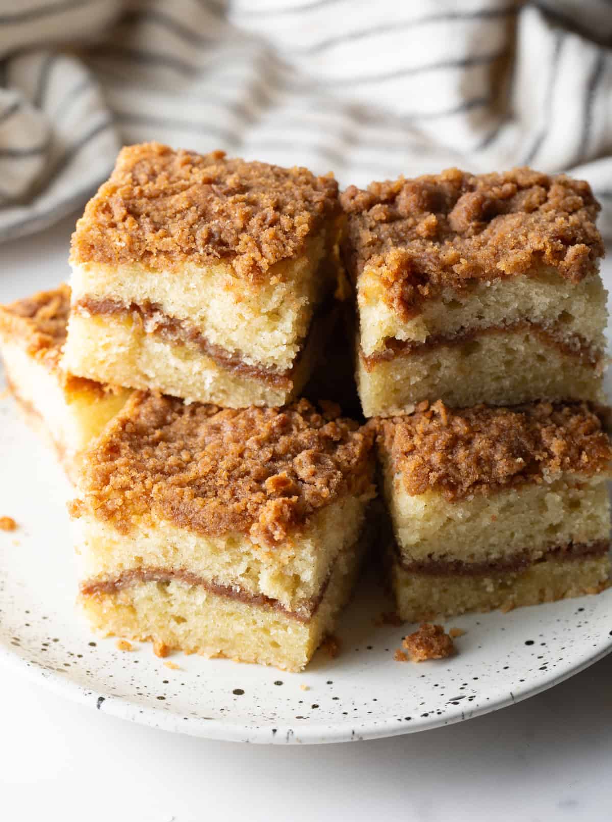 Several slices of cinnamon breakfast cake are stacked on top of each other on a white plate.