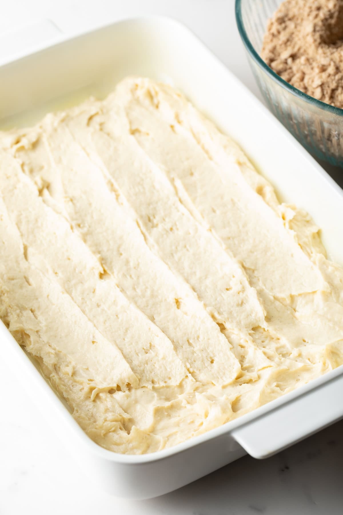 A white baking pan is filled halfway with sour cream coffee cake mixture.