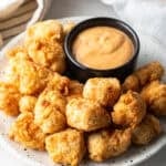 A white plate filled with fried fish nuggets next to a ramekin of dipping sauce.