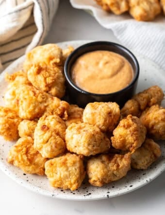 A white plate filled with fried fish nuggets next to a ramekin of dipping sauce.