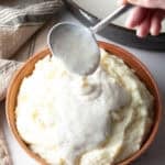 A white gravy recipe is being spooned over a bowl of mashed potatoes.
