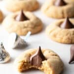 Peanut butter blossoms recipe arranged on white parchment paper, and the cookie closest to the camera has a bite taken out of it.