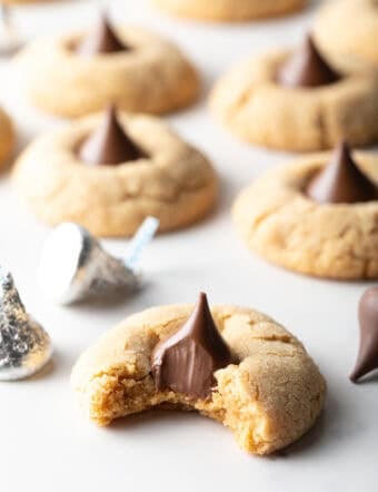 Peanut butter blossoms recipe arranged on white parchment paper, and the cookie closest to the camera has a bite taken out of it.